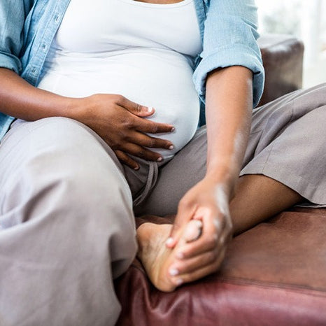 barefoot and clothed pregnant woman gripping her belly and left foot