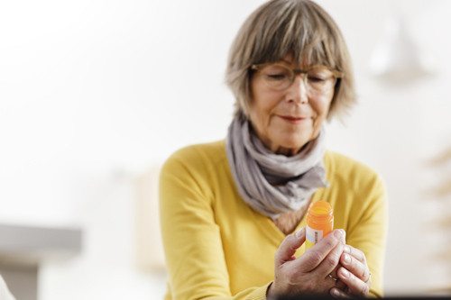 elderly woman looking concerned reading the label on her medicine bottle